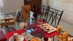 Una mesa de cristal con manteles individuales rojos y una variedad de alimentos, entre ellos frutas, pasteles y bebidas.