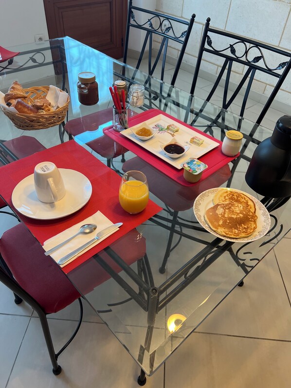 A breakfast setting with a glass table, red placemats, and various breakfast items including pancakes, orange juice, and condiments. - Le Médoc de Clémence (Lamarque)