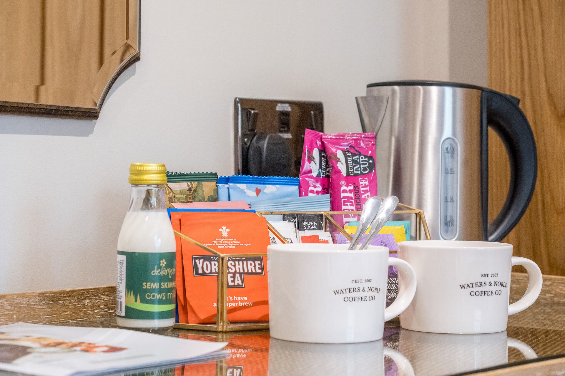 A kitchen counter with a coffee maker, a bottle of milk, tea bags, and coffee mugs.