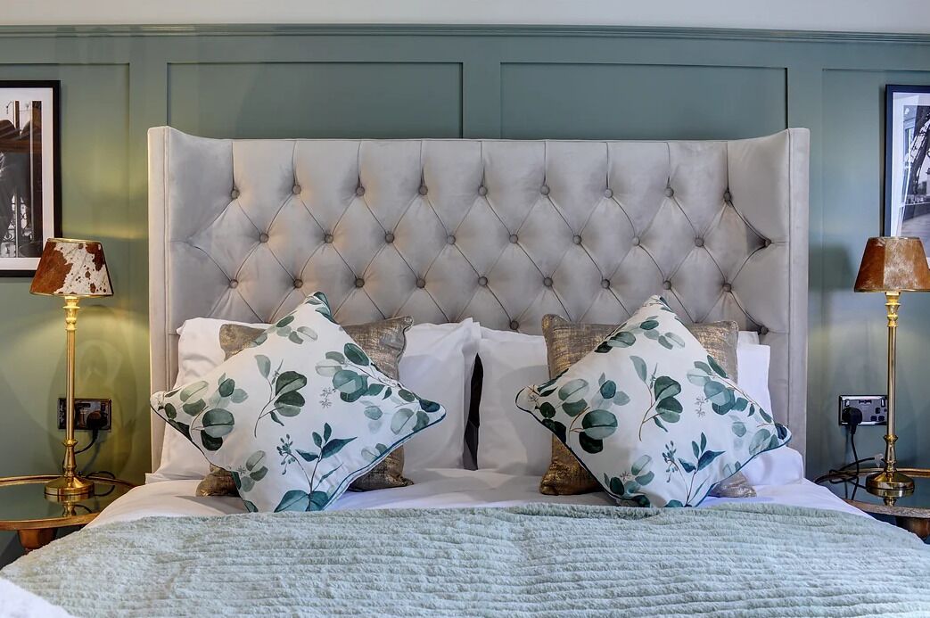 A bed with a tufted headboard, two floral pillows, a white duvet, and a light blue blanket.
