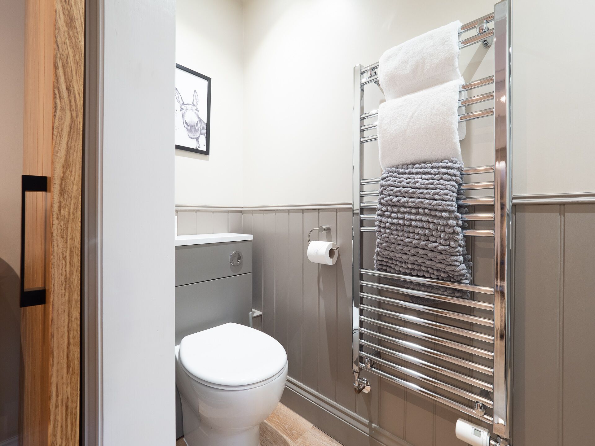 A bathroom with a toilet, a towel rack with towels, a framed picture on the wall, and a toilet paper holder.