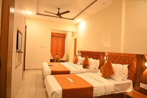 A hotel room with two beds, a ceiling fan, a small table with chairs, and a window with curtains. - Hotel Embassy INN (Ujjain)