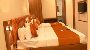 Quarto de hotel com uma cama grande, cabeceira de madeira, duas mesas de cabeceira, um ventilador de teto e uma TV fixada na parede.