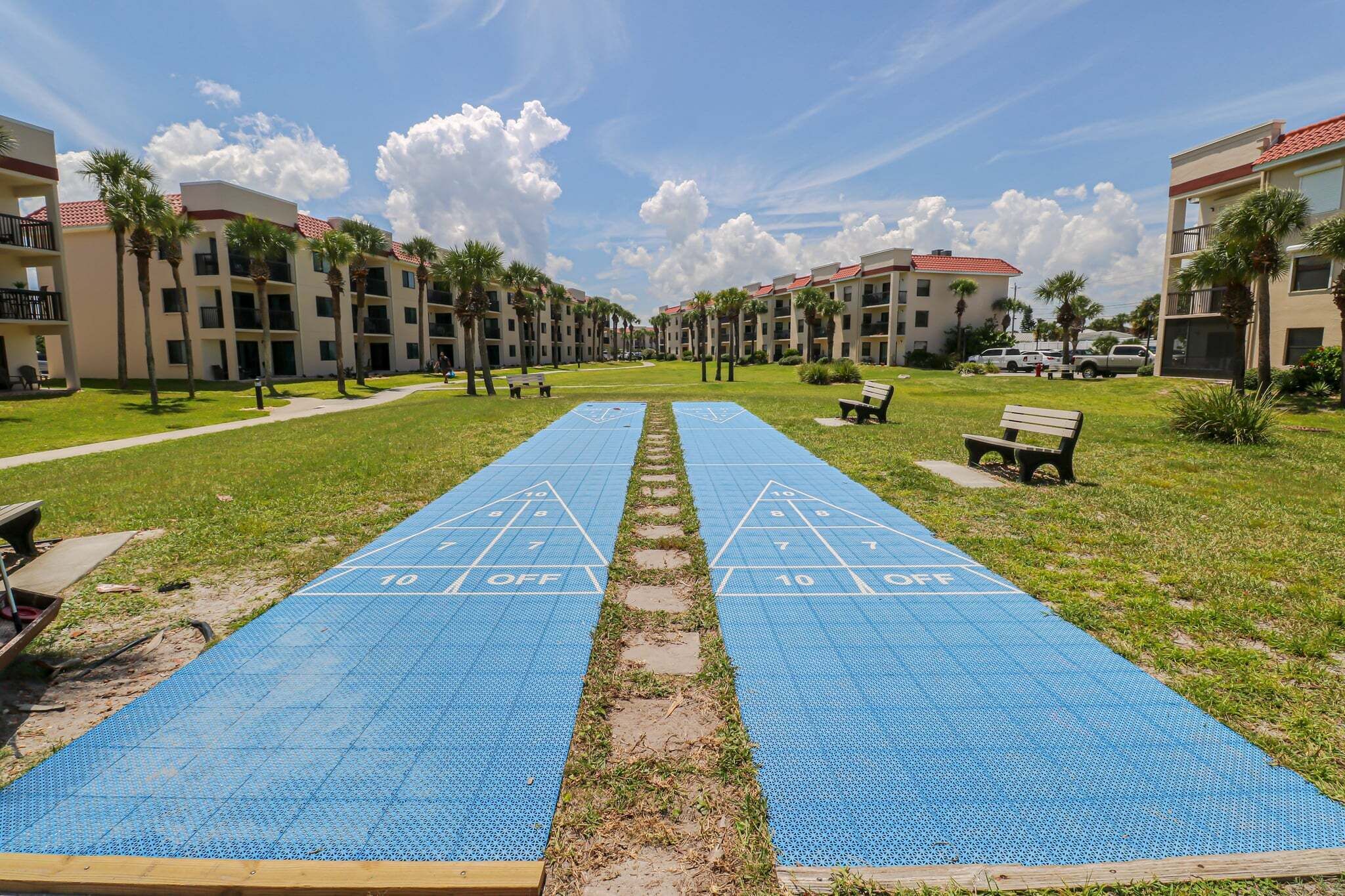 Uma quadra de shuffleboard num pátio com céu claro, rodeada por edifícios com varandas.