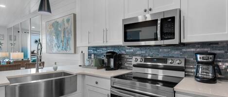 A modern kitchen with stainless steel appliances, white cabinetry, and a blue-tiled backsplash.
