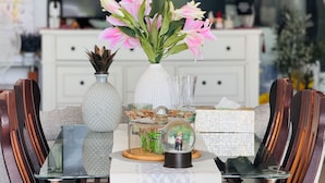 Una mesa de comedor con un florero de flores rosas, una esfera de cristal decorativa y una pequeña figurita.