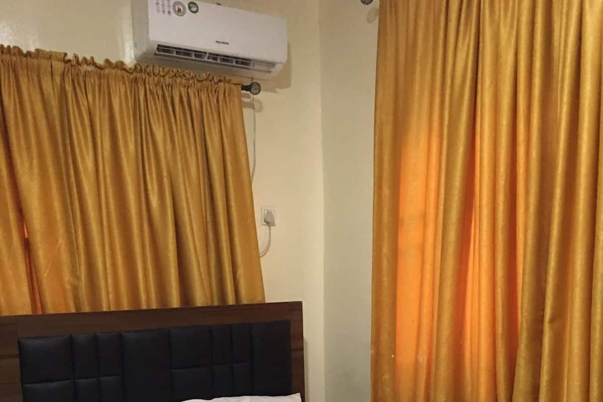 A neatly made bed with white linens, a dark headboard, and a wall-mounted air conditioner.
