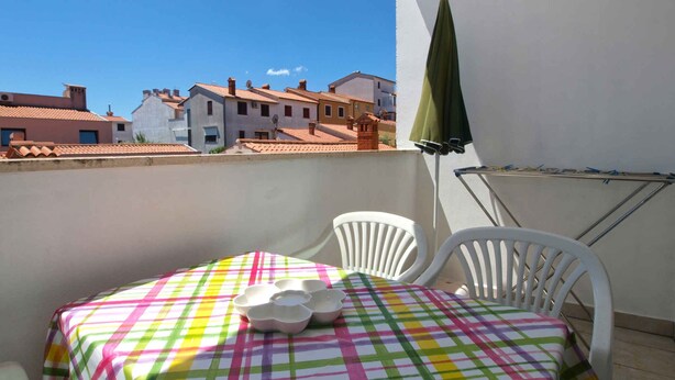 A balcony with a table and chairs, a green umbrella, and a view of buildings. - Holiday apartment with air conditioning (Pula)