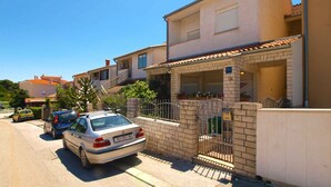 A residential street with a parked car, a gated entrance, and a building with a tiled roof. - Holiday apartment with air conditioning (Pula)