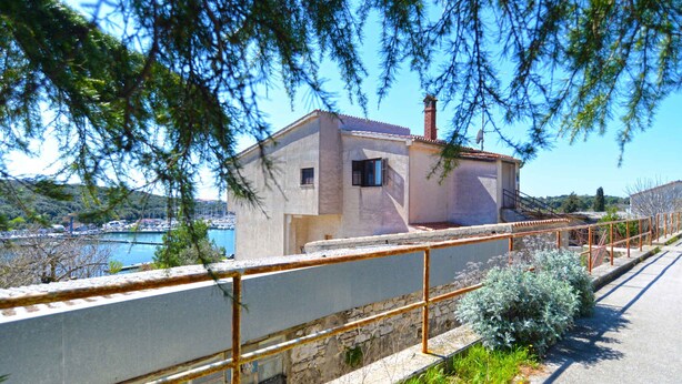 Un bâtiment situé sur la côte, doté d’un mur en pierre et d’une rambarde en métal, et offrant une vue sur une étendue d’eau.