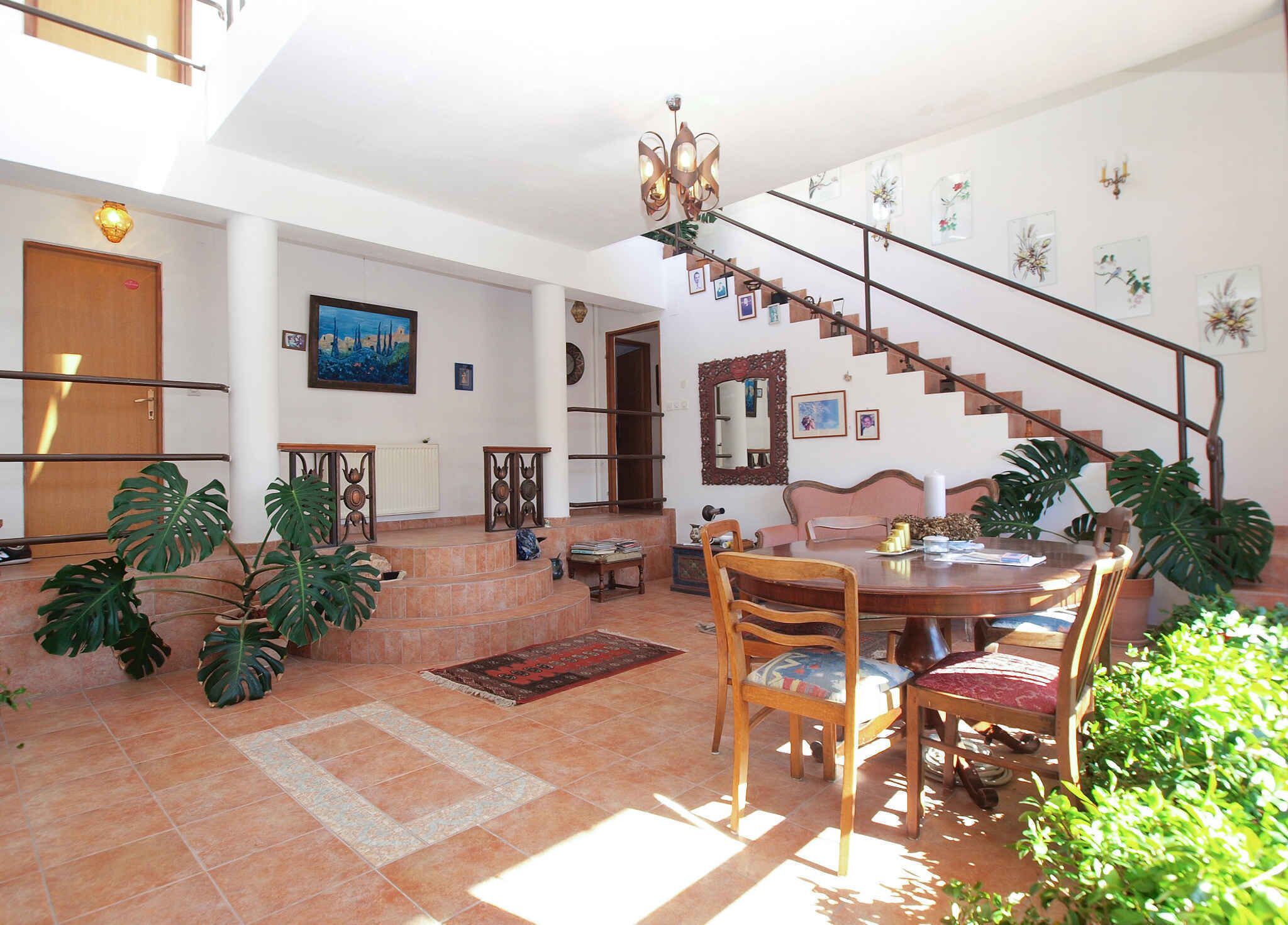 A spacious living area with a dining table, chairs, a staircase, and various plants.