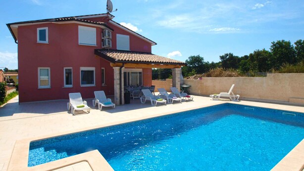A red villa with a swimming pool, outdoor seating, and a pergola.