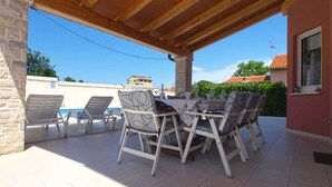 An outdoor patio with a wooden ceiling, white tiled floor, and a table set for dining.