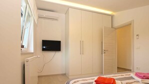 A bedroom with a bed, a TV mounted on the wall, a radiator, and a wardrobe.
