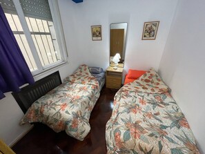 Un dormitorio con dos camas individuales, un aparador, un espejo y una ventana con barrotes.
