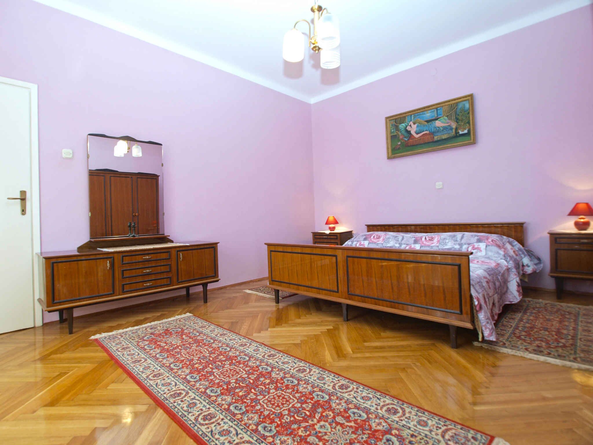 Een slaapkamer met een houten bed, nachtkastje, dressoir, spiegel en vloerkleed.
