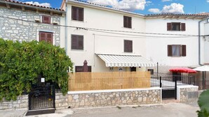 Un bâtiment à deux étages, avec une façade en pierre et en crépi, une clôture en bois et un parasol rouge.