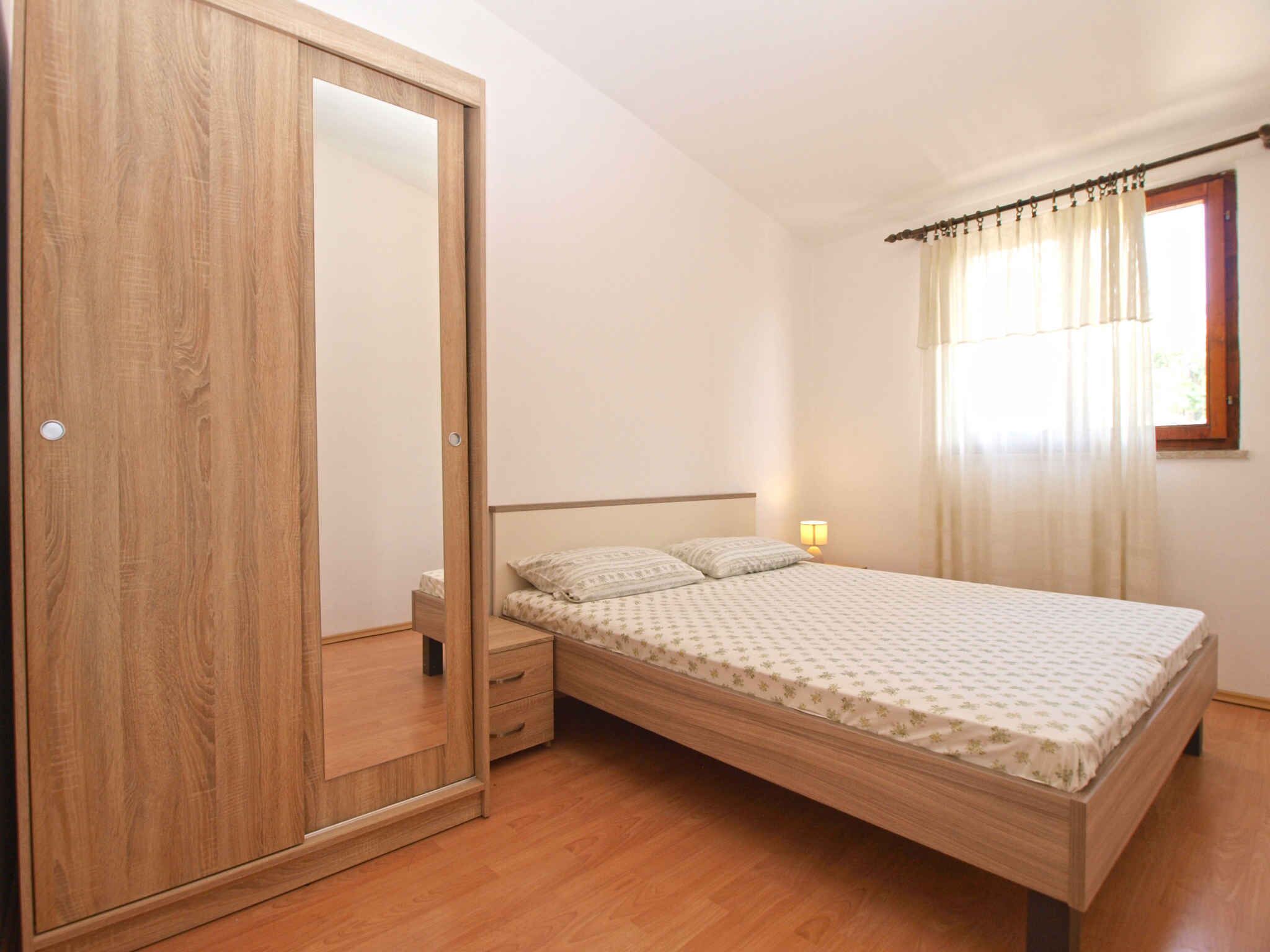 Un dormitorio con un armario de madera, una cama con colcha estampada, una mesita de noche con lámpara y una ventana con cortinas.