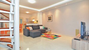 A modern living room with a grey sectional sofa, a colorful rug, a flat-screen TV on a wooden stand, and a staircase with wooden railings. - Holiday apartment with air conditioning (Pula)