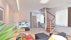 A modern living room with a flat-screen TV, grey sofas, a colorful rug, and a wooden staircase. - Holiday apartment with air conditioning (Pula)