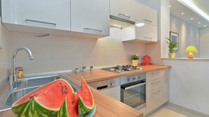 A modern kitchen with white cabinets, a wooden countertop, a sink, a stove, and a small potted plant. - Holiday apartment with air conditioning (Pula)