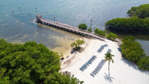 Luchtbeeld van een strand met een pier die zich uitstrekt over het water, omringd door weelderige begroeiing.