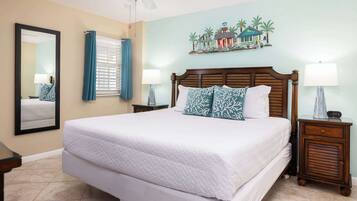 A hotel room with a large bed, a wooden headboard, a nightstand with a lamp, a mirror, and a wall with a tropical mural.