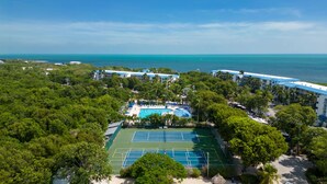 Luchtbeeld van een resort met een tennisbaan, zwembad en uitzicht op zee.