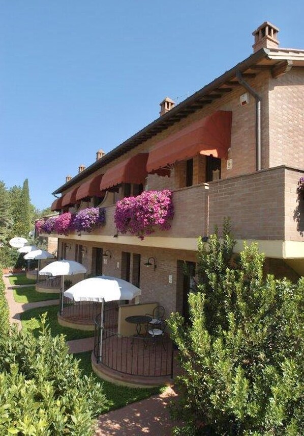 A hotel with a brick facade, outdoor seating with umbrellas, and flower boxes on the balcony. - Holiday-Home with pool in San Gimignano (San Gimignano)