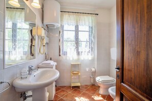 A bathroom with a sink, toilet, and mirror. There is a window with curtains and a shelf with towels. - Holiday-Home with pool in San Gimignano (San Gimignano)