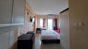Habitación de hotel con cama, escritorio, silla, equipo de aire acondicionado y ventana con cortinas.