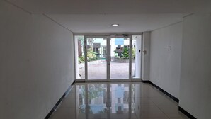 Un pasillo con una puerta de cristal que da al exterior, suelo de baldosas y paredes blancas.