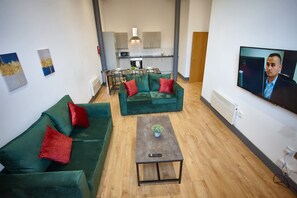 Un salon avec un canapé vert, une table basse et un téléviseur qui diffuse une émission mettant en scène une personne.