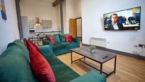 Ein modernes Wohnzimmer mit einem grünen Sofagarnitur, einem Couchtisch und einem an der Wand befestigten Fernseher.