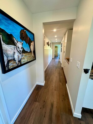 A hallway with wooden flooring, white walls, and a large painting of animals. - 4TreesVA: Old Rag Mountain Retreat (Etlan)