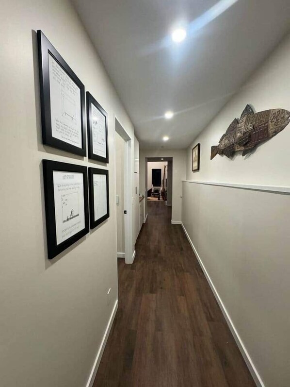 Un couloir aux murs ornés de cadres contenant des certificats, un plancher en bois et une porte au fond.