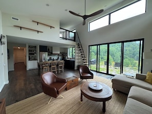 A spacious living area with a high ceiling, a dining area, and a kitchen. There is a large window providing a view of the outdoors. - Quiet, Pet-friendly, Mountain Escape Near Wineries & Hiking (Etlan)