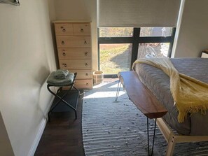 A bedroom with a bed, a wooden dresser, a small table, and a window with a view of the outdoors. - 4TreesVA: Old Rag Mountain Retreat (Etlan)
