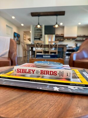Une pile de livres sur une table, dans une pièce dont on aperçoit un coin repas à l’arrière-plan.