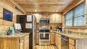 Una cocina moderna con muebles de madera, encimeras de granito, electrodomésticos de acero inoxidable y una ventana con persianas.