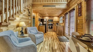 Interior acogedor de una cabaña con paredes de madera, una zona de cocina y dos sillones grises.