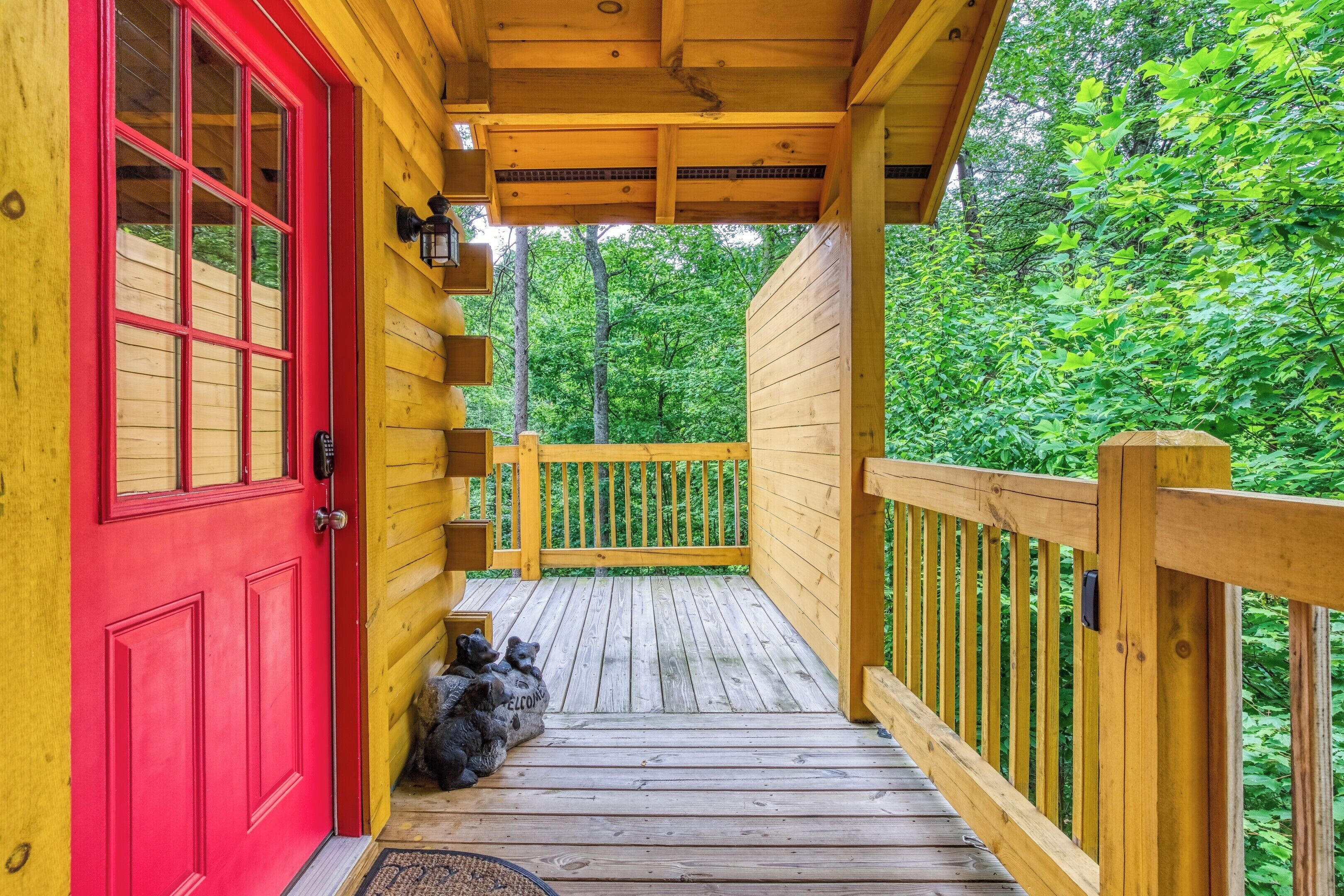 A wooden deck with a red door, a wooden railing, and a view of a forest.