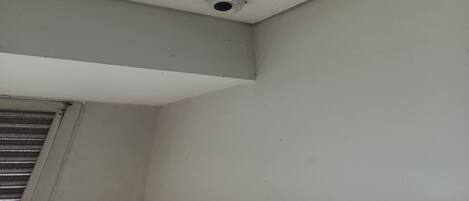 A corner of a room with a ceiling vent and a window with horizontal blinds.