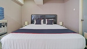 Une chambre d’hôtel avec un lit, des tables de chevet, un distributeur d’eau et une porte.