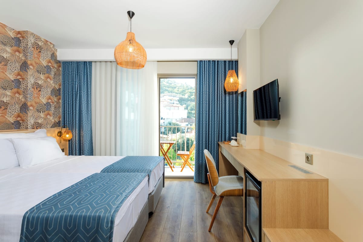 A hotel room with a bed, desk, chair, TV, and a balcony with a view.