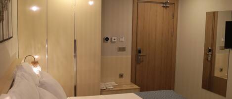 A hotel room with a bed, bedside table, lamp, wardrobe, and a mirror.