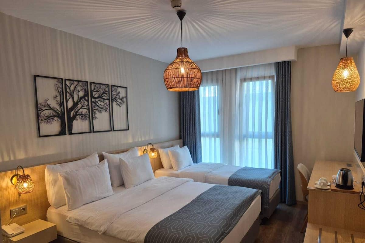 A hotel room with two beds, a desk, a chair, and a large window with curtains.