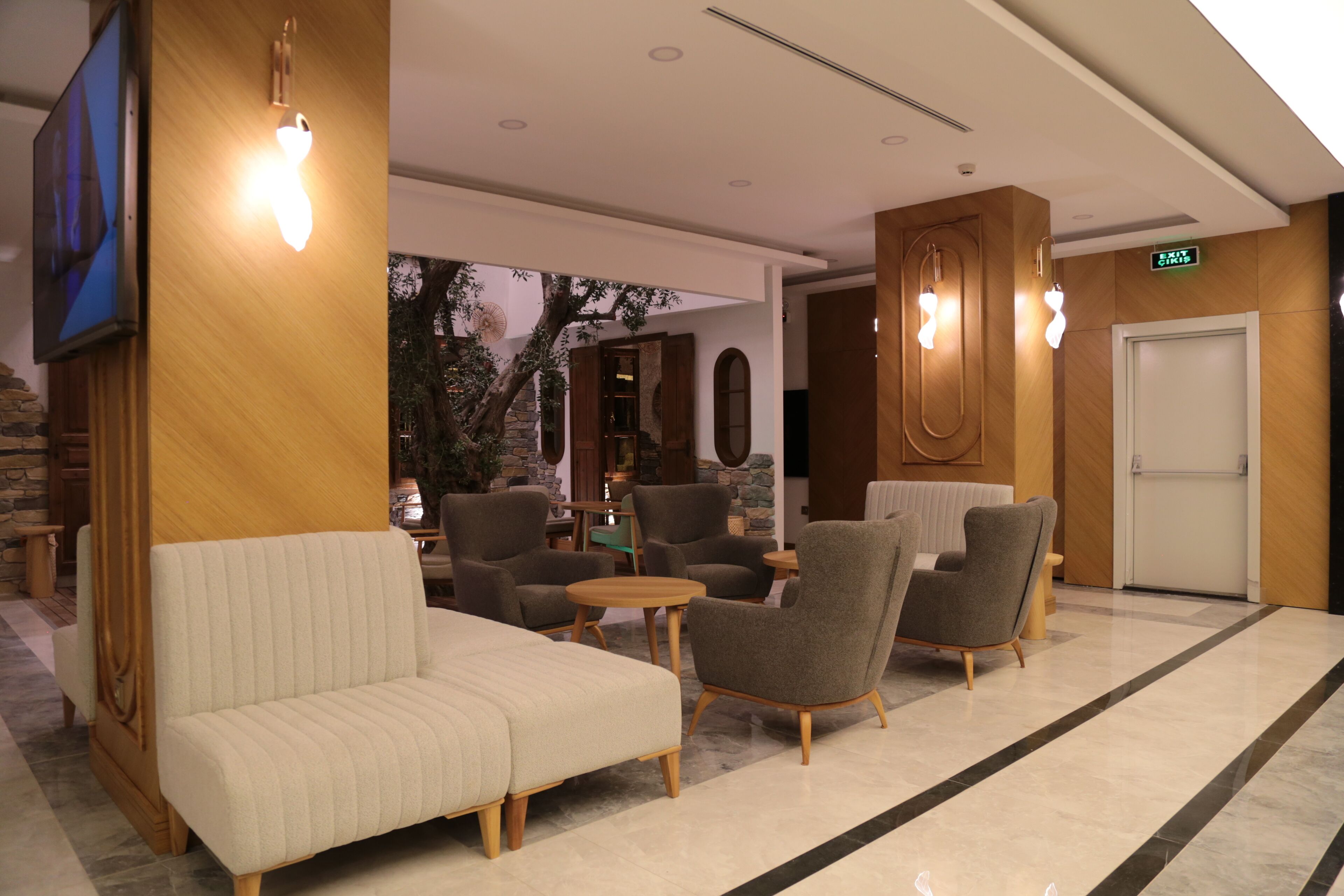 A lobby with a sofa, armchairs, a TV, and a reception desk.