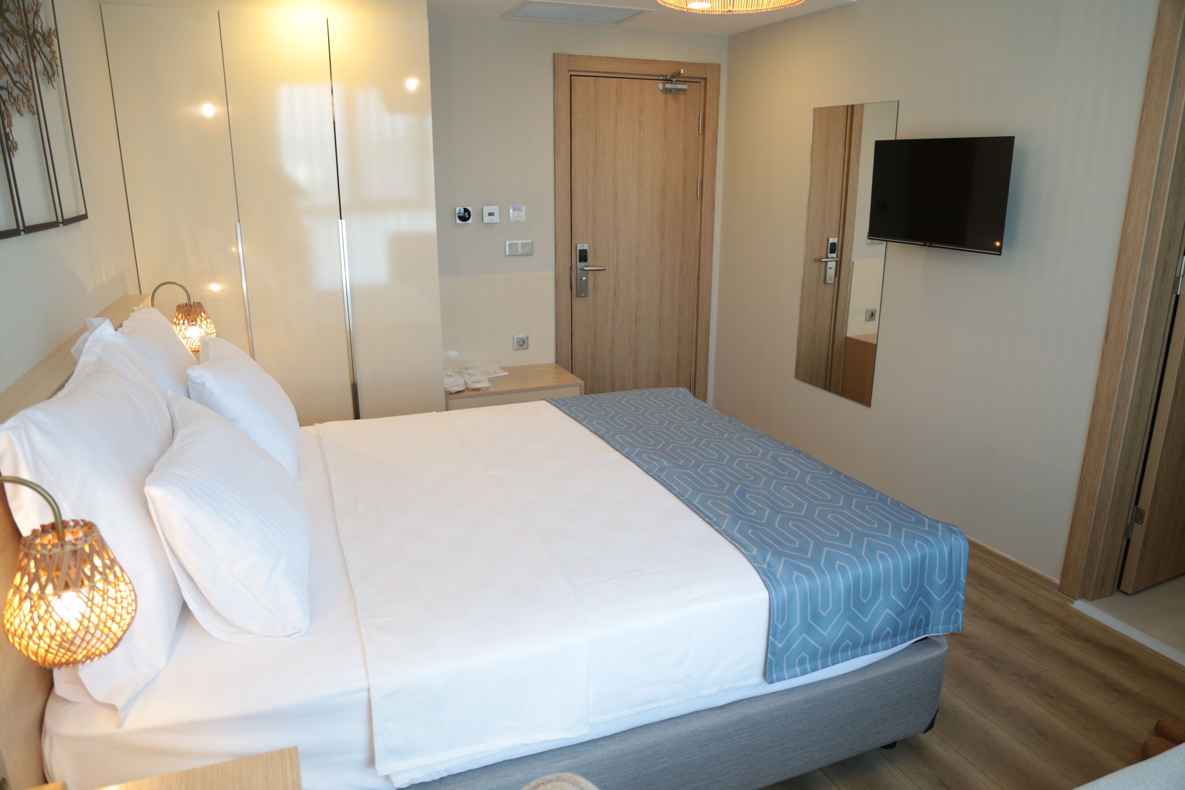 A hotel room with a large bed, bedside tables, a TV mounted on the wall, and a wooden door.