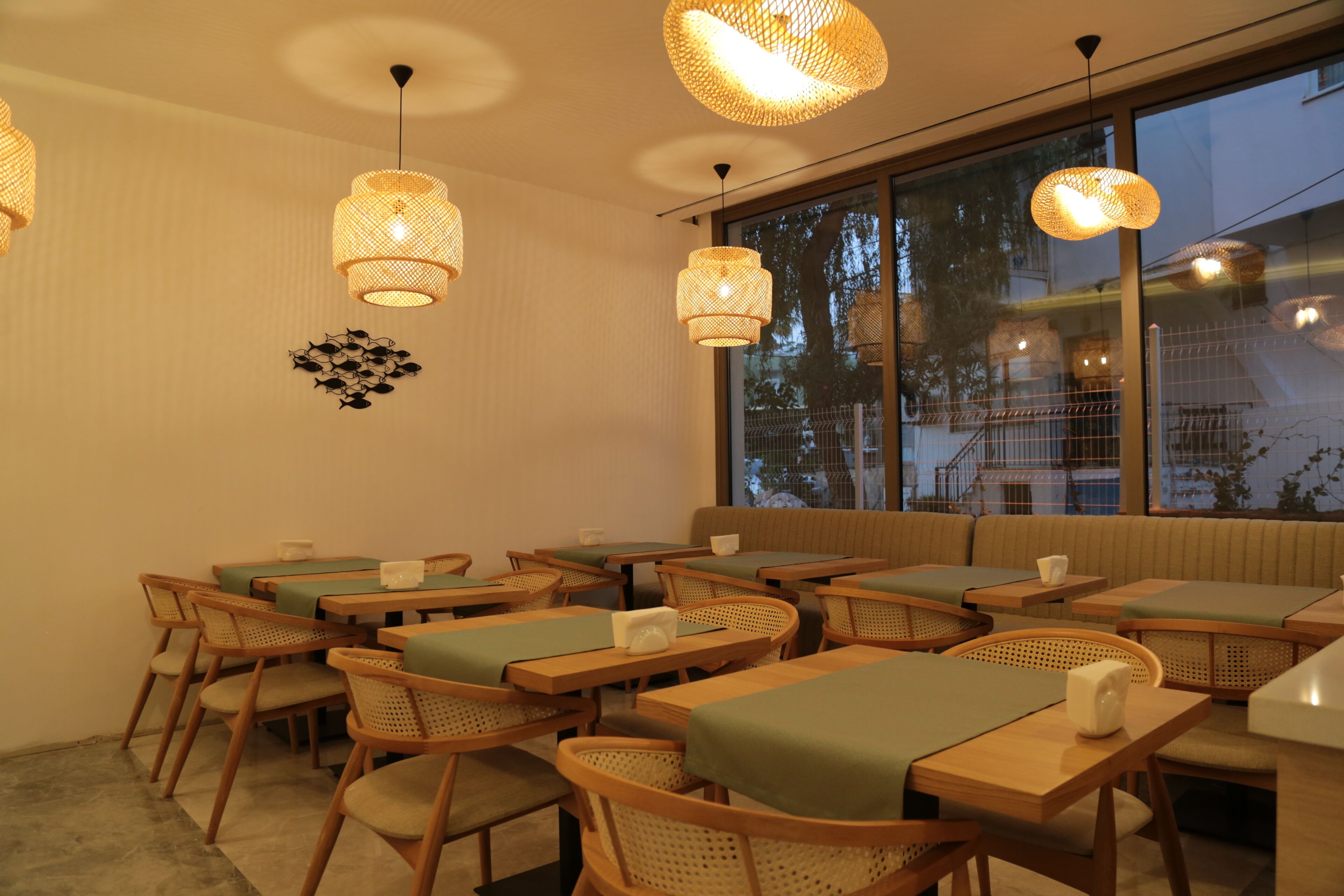 Un restaurante con mesas y sillas de madera, manteles verdes y lámparas colgantes de mimbre.